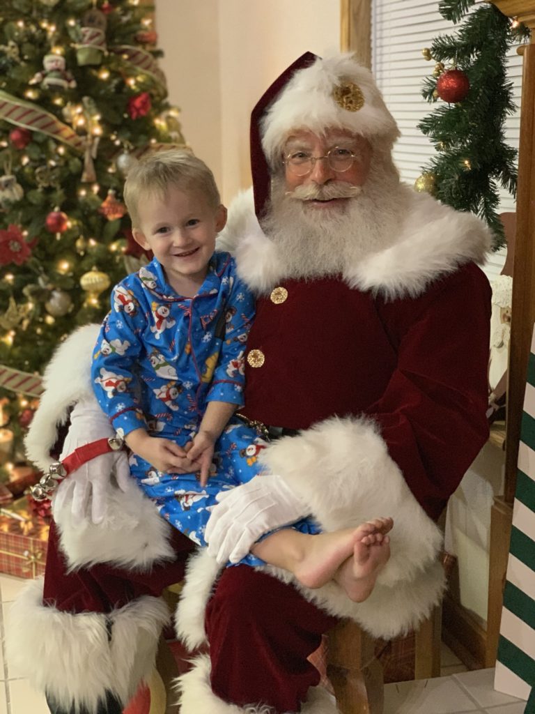 Santa Jim with a small boy in blue pajamas on his knee